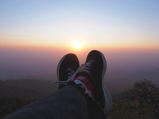 Tourist selfie feet over sunrise sky background on the high mountain.