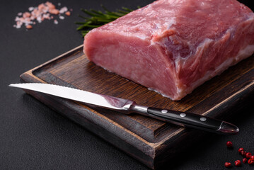 A piece of raw fresh pork on a wooden cutting board with spices and herbs