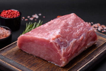 A piece of raw fresh pork on a wooden cutting board with spices and herbs