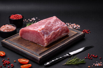 A piece of raw fresh pork on a wooden cutting board with spices and herbs