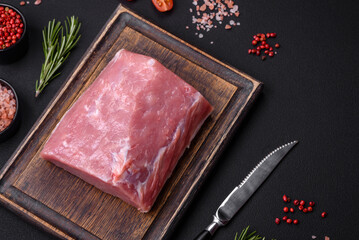 A piece of raw fresh pork on a wooden cutting board with spices and herbs