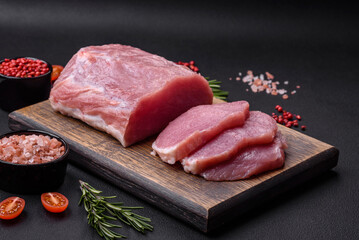 A piece of raw fresh pork on a wooden cutting board with spices and herbs