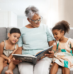 Family, grandmother and children with book reading on sofa for bonding, relaxing and quality time together. Love, education and elderly woman with girls learn to read story, fairy tale and literature