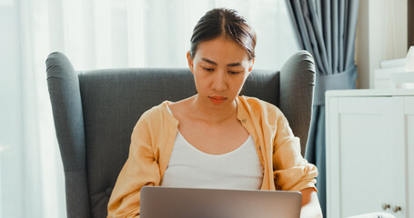 Young attractive asian female girl or university student sit on sofa chair with computer laptop...