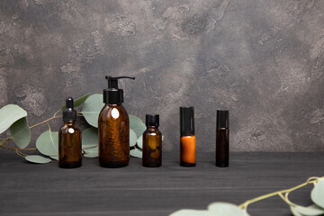 Amber bottles with facial cosmetics with a branch of eucalyptus on the dark wooden and concrete background