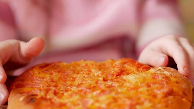 Close-up, the child's hands near a slice of pizza lying on the table.