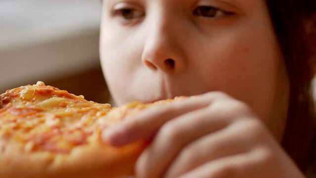 A little girl bites off a piece of pizza in close-up. The concept of improper nutrition. Selective focus.