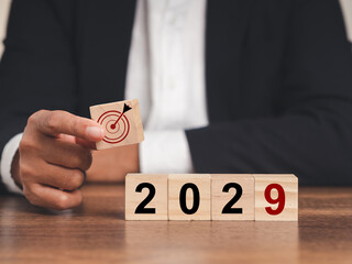 Business planning and strategy in 2029. Hand businessman holding wooden cubes with dartboard icon...