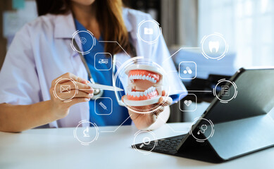 Concentrated dentist sitting at table with jaw samples tooth model and working with tablet and laptop in dental office professional dental clinic..
