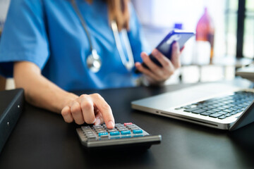 Healthcare costs and fees concept.Hand of smart doctor used a calculator and smartphone, tablet for medical costs at hospital in morning light.