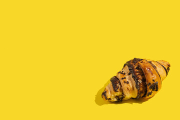 Fresh chocolate croissant on yellow background with copy space.