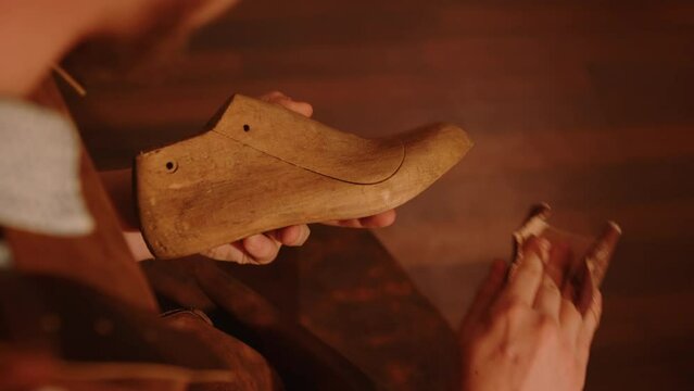 Craftsman grinds wooden shoe last with sandpaper in shoemaker workshop. Handmade shoe making. 