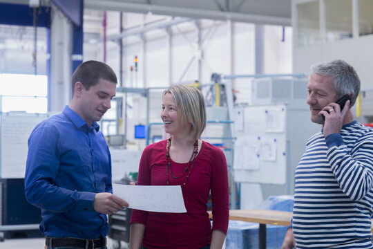 Business man holding document while taking to business woman and colleague talking on phone at office