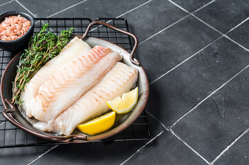 Fresh raw cod fish fillets with herbs served on steel tray. Black background. Top view. Copy space
