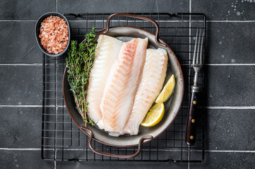 Fresh raw cod fish fillets with herbs served on steel tray. Black background. Top view