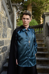 Obraz premium Close up portrait of handsome brunette man wearing fantasy medieval prince costume with golden crown and romantic silk shirt. historical castle location background.
