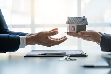 Young Asian real estate agent, and insurance salesman handing over a sample house to a client after signing the sale at the office. - obrazy, fototapety, plakaty