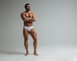 Sexy muscular man in white underwear posing in studio. Handsome bodybuilder standing on grey background. Big male model showing his muscles. - Powered by Adobe
