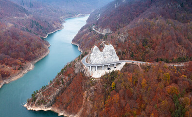 Amazing aerial view of a cliff coast road through mountains and autumn forests next to a lake Siriu...