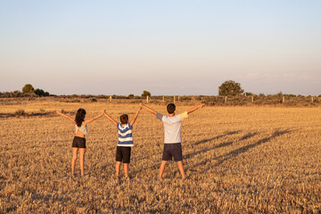 Three kids with open arms on a field at sunset