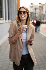 Attractive businesswoman drinking a coffee and using a mobile while enjoying break
