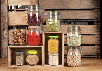 Home pantry. Natural and sustainable food, eco-friendly. Canned tomatoes, nuts, green beans, kidney beans, split peas, pasta, rice, chickpeas. Glass jars on wooden boxes.