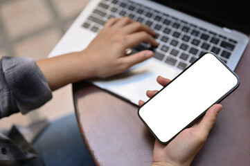 Top view of a female holding a smartphone white screen mockup while remote working