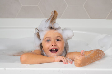 Kid in a bath tub. Washing in bath with soap suds on hair. Child taking bath. Closeup portrait of smiling kid, health care and kids hygiene. Kids face in bath tub with foam.