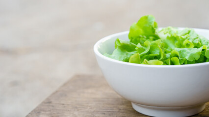 Green vegetables or lettuce in white bowl on wooden background. Healthy food concept.