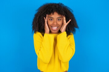 Fototapeta na wymiar young woman with afro hairstyle wearing orange crop top over blue wall Pleasant looking cheerful, Happy reaction