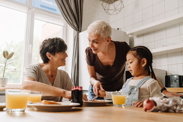 Two smiling mature women with little asian girl eating toasts