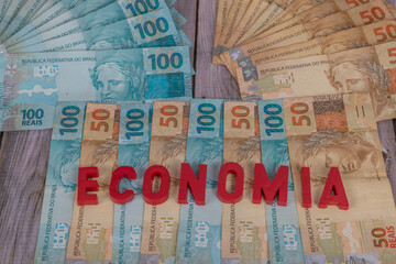 50 and 100 reais banknotes on wood, written "economia" in Portuguese. Selective focus.