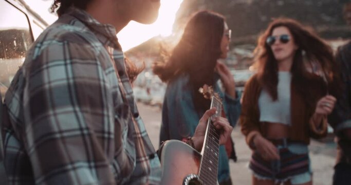 Multi-ethnic group of hipster friends singing and dancing with a guitar at the harbor on sunset