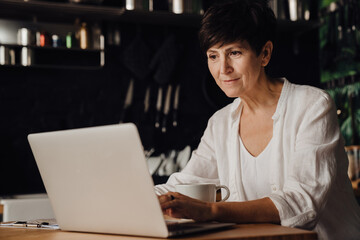 Mature woman working on laptop computer while sitting at home