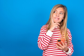 Image of a thinking dreaming caucasian teen girl wearing striped shirt over blue studio background...