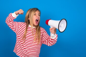 caucasian teen girl wearing striped shirt over blue studio background communicates shouting loud holding a megaphone, expressing success and positive concept, idea for marketing or sales.