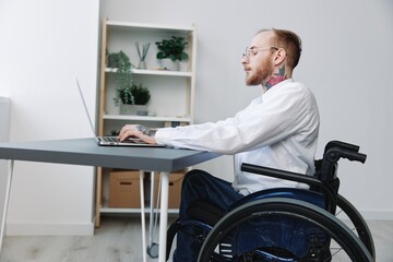 A man wheelchair businessman with tattoos office works at a laptop online, social networks and...