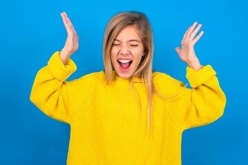caucasian teen girl wearing yellow sweater over blue studio background goes crazy as head goes...