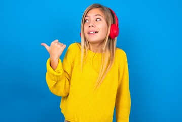 caucasian teen girl wearing yellow sweater over blue studio background listens audio track via...