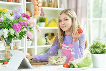 Obraz na płótnie Canvas girl preparing fresh salad on kitchen table with tablet at home