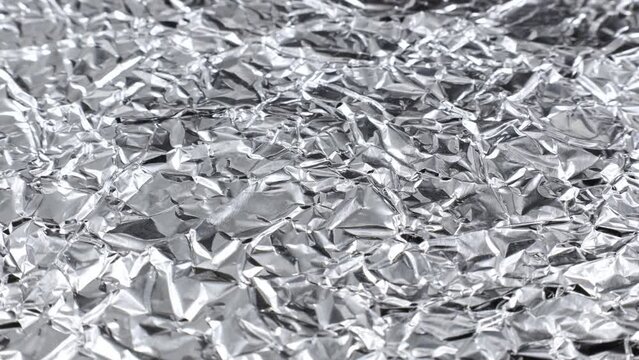 Wrinkled silver colored shiny aluminum foil texture circle rotation close up