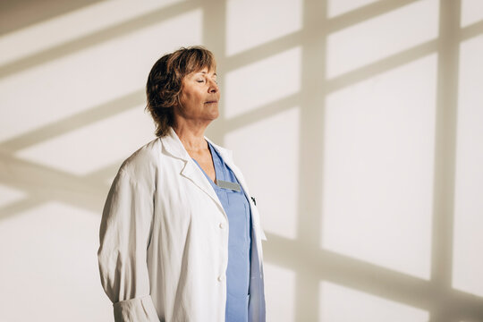 Mature female physician standing with eyes closed against wall with shadow