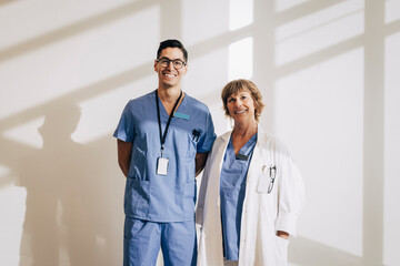 Portrait of happy doctor standing with nurse against wall at hospital