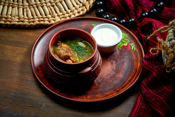 Traditional Ukrainian green borscht with meat and sour cream in a clay pot.