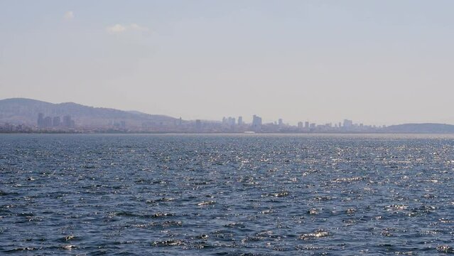 Asian shore of Istanbul, view of Maltepe and Kartal from sailing ferry boat. Sunny summer day, city buildings and hills seen from distance. Little waves sparkling in sunlight in the foreground