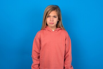 Fototapeta premium Offended dissatisfied beautiful caucasian teen girl wearing pink sweater over blue wall with moody displeased expression at camera being disappointed by something