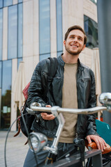 Fototapeta premium Cheerful man using mobile phone while standing with bicycle outside