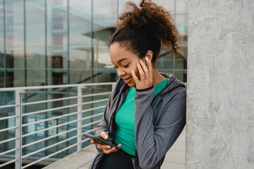 Smiling african girl listening music with earphones and mobile phone while standing outdoors