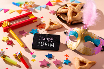Purim table with hamantaschen cookies, carnival mask, Happy Purim quote, holiday decor in hard light