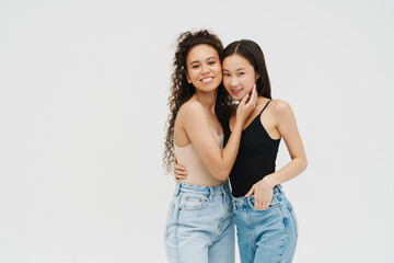 Fototapeta premium Two cheerful girls hugging while posing isolated over white wall